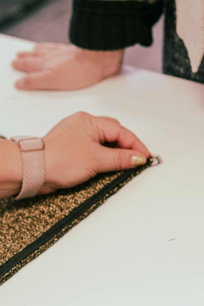 Leim Sewing Workshops - Jumpsuit Sewing Workshops - a white woman is holding a black zip against the edge of her sparkly golden fabric while another woman leans on the table and watches